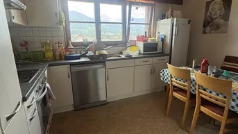Gemütliche Küche mit Essbereich, weißen Schränken, Holzdecke und Bergblick durch das Fenster.