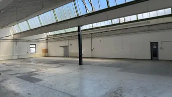 Große, leere Lagerhalle mit hohen Decken und Oberlichtern, ideal für industrielle Nutzung.