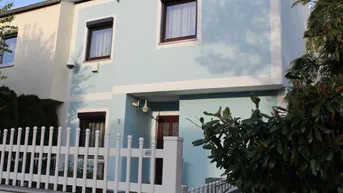 Vorderansicht eines Reihenhauses mit hellblauer Fassade, weißen Fensterrahmen und einem weißen Zaun.