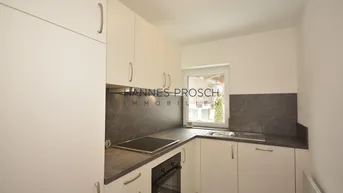 Kleine, moderne Küche mit weißen Schränken, dunkler Arbeitsplatte und Fenster für Tageslicht.