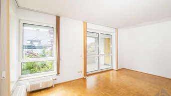 Helles Wohnzimmer mit Parkettboden, großem Fenster und Zugang zu einem Balkon.