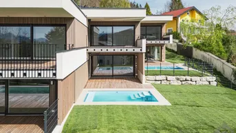 Moderne Architektur mit mehreren Pools, weitläufigen Rasenflächen und Bergblick in grüner Umgebung.