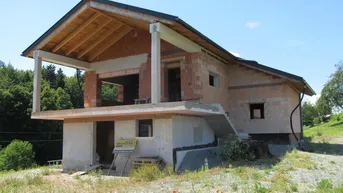 Rohbau eines Einfamilienhauses in ländlicher Umgebung mit sichtbarer Holzkonstruktion des Daches.