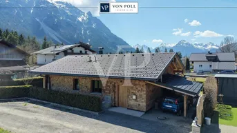 Modernes Holzhaus mit Schindelfassade und Carport vor beeindruckender Bergkulisse.