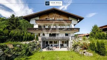 Traditionelles Alpenhaus mit mehreren Balkonen und einer Terrasse im Grünen, umgeben von Bergen.