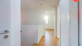 Heller Flur mit Holzparkettboden, Oberlicht und Treppenaufgang, der viel Tageslicht hereinlässt.