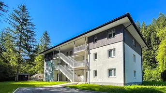 Modernes Mehrfamilienhaus mit Außentreppen und Balkonen, umgeben von grüner Natur und Bäumen.