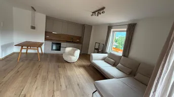Heller offener Wohn- und Essbereich mit moderner Küche und Holzboden, bietet einen grünen Ausblick.