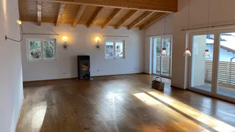 Geräumiges Wohnzimmer mit Holzbalkendecke, Kaminofen und Zugang zum Balkon.