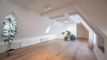Weitläufiges Dachgeschoss-Wohnzimmer mit Holzboden, schrägen Wänden und mehreren Dachfenstern.