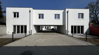 Moderne weiße Fassade eines Neubaus mit Durchfahrt und großen Fenstern unter blauem Himmel.
