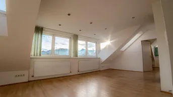 Helles, leeres Zimmer im Dachgeschoss mit Holzfußboden, Dachschrägen und großen Fenstern mit Ausblick.