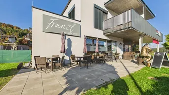 Außenansicht des Cafés mit möblierter Terrasse und Blick auf die umliegende Landschaft.