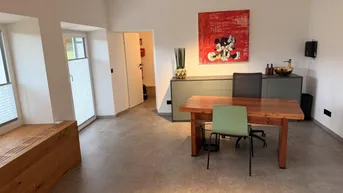 Heller Büroraum mit modernem Schreibtisch, Sitzgelegenheiten und einem kleinen Waschbeckenbereich.