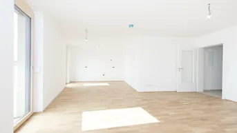 Helles, leeres Zimmer mit Parkettboden und Zugang zu einem Balkon oder einer Terrasse.