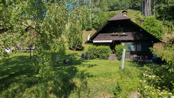 Traditionelles Holzhaus mit Satteldach und großem Garten in grüner Hanglage, umgeben von Bäumen.