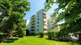 Mehrfamilienhaus mit gepflegter Grünanlage und Kinderspielplatz unter blauem Himmel.