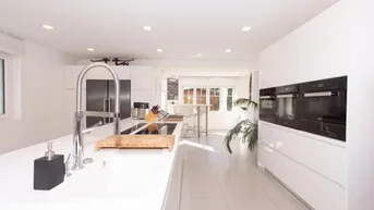 Moderne, helle Küche mit Kochinsel, integrierten Geräten und weißen Hochglanzfronten.