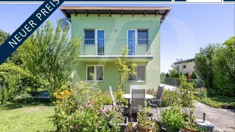 Haus mit hellgrüner Fassade, Balkon und gemütlicher Terrasse im blühenden Garten.