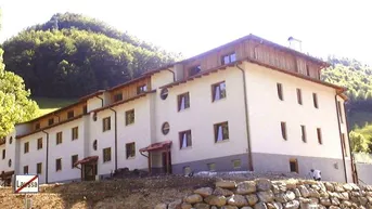 Mehrstöckiges Gebäude mit heller Fassade und Holzelementen in einer grünen Berglandschaft.