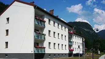 Modernes Mehrfamilienhaus mit Balkonen und Blick auf die umliegenden Berge und grüne Landschaft.