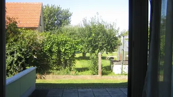 Blick von der Terrasse auf den grünen Garten mit Bäumen und angrenzendem Haus.