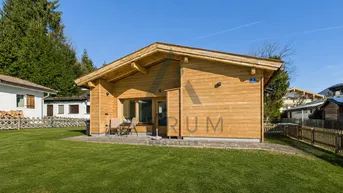 Modernes Holzhaus mit kleiner Terrasse und gepflegtem Rasen in sonniger Lage.
