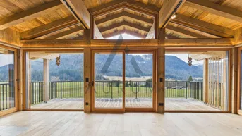Geräumiger Wohnbereich mit hohen Holzdecken, großen Glasfronten und weitem Blick auf die Berge.
