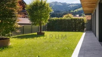 Gepflegter Gartenbereich mit Rasen, Bäumen und Hecke, mit Blick auf die umliegende Berglandschaft.
