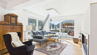 Helles Wohnzimmer mit bequemen Sofas, Kamin und großen Fenstern mit Bergblick.