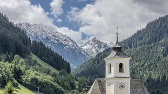 Malerische Berglandschaft mit schneebedeckten Gipfeln und einer charmanten Kirche im Tal.