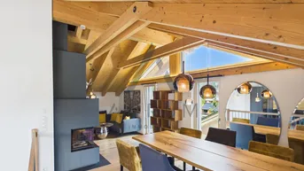 Heller Wohn- und Essbereich mit Holztisch, modernen Pendelleuchten und integriertem Kamin.