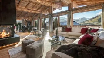 Großzügiger Wohn- und Essbereich mit Kamin, Holzbalkendecke und Panoramablick auf die Berge.