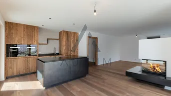 Moderne offene Küche mit Holzelementen, dunkler Kochinsel und integriertem Kamin im Wohnbereich.