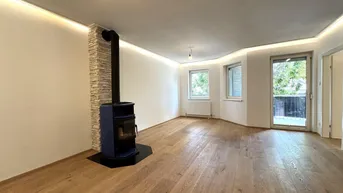 Geräumiges Wohnzimmer mit modernem Holzofen, Holzboden und Zugang zum Balkon.