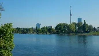Weitläufiger Blick über einen See mit Stadtpanorama und einem Fernsehturm im Hintergrund.