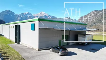 Luftaufnahme eines modernen Gewerbegebäudes mit Laderampe und beeindruckendem Alpenpanorama im Hintergrund.