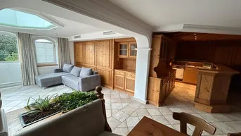 Geräumiger Wohn- und Essbereich mit traditionellen Holzmöbeln, Fliesenboden und viel Tageslicht durch große Fenster.
