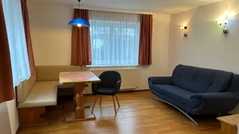 Gemütlicher Wohn- und Essbereich mit Holzboden, Sitzbank und Sofa, ideal für gesellige Stunden.