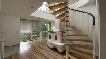 Geräumiges Wohnzimmer mit Holzboden, Wendeltreppe und traditionellem Kachelofen. Große Fenster bieten viel Tageslicht.