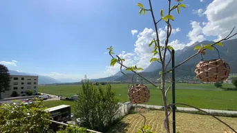 Weitläufiger Blick über grüne Felder und majestätische Berge unter strahlend blauem Himmel.