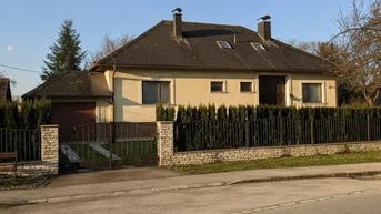 Hausansicht von der Straße mit Vorgarten und Zaun unter blauem Himmel.