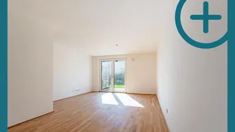 Helles, leeres Zimmer mit Parkettboden und Zugang zu einem kleinen Gartenbereich.