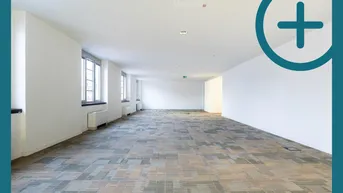 Großer, leerer Büroraum mit gemustertem Teppichboden und mehreren Fenstern, die natürliches Licht hereinlassen.