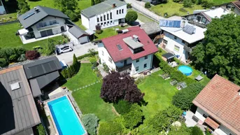 Luftaufnahme einer Wohnsiedlung mit grünen Gärten, Bäumen und einem Swimmingpool.