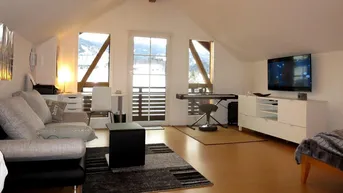 Geräumiger Wohnbereich im Dachgeschoss mit Holzboden, Sofa und Zugang zum Balkon.