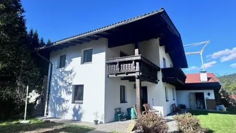 Traditionelles weißes Haus im alpenländischen Stil mit Holzbalkonen und gepflegtem Vorgarten.
