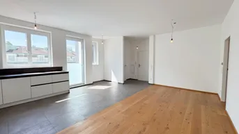 Heller offener Wohnbereich mit Parkettboden, Fliesen und vorbereiteter Küchenzeile, ideal für modernes Wohnen.