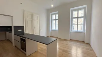 Moderne Küche mit Kochinsel und Holzboden, offen zum Wohnbereich mit hohen Fenstern.