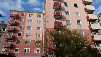 Mehrstöckiges Wohngebäude mit rosa Fassade und roten Balkonen unter blauem Himmel.